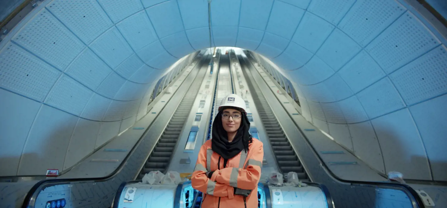 Female engineer stands proudly in front of underground escalators