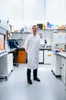 George Frodsham, male chemical engineer, smiles at camera and stands in a laboratory 