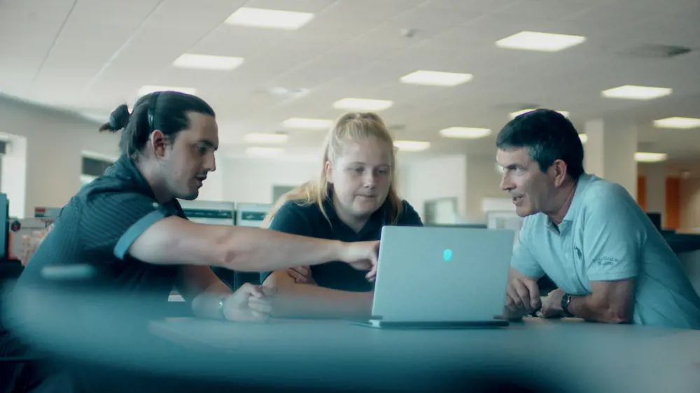 One female and two male engineers discussing ideas around a laptop