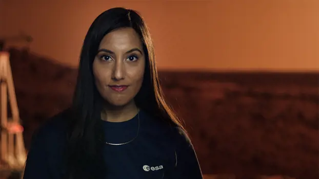 Close up of Vinita looking straight ahead in front of a red replica Mars surface