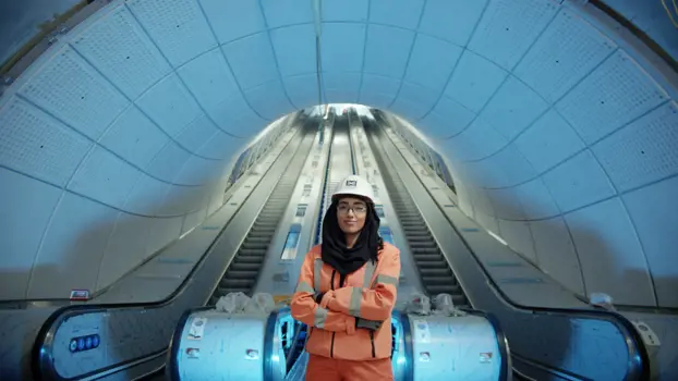 Female engineer stands proudly in front of underground escalators
