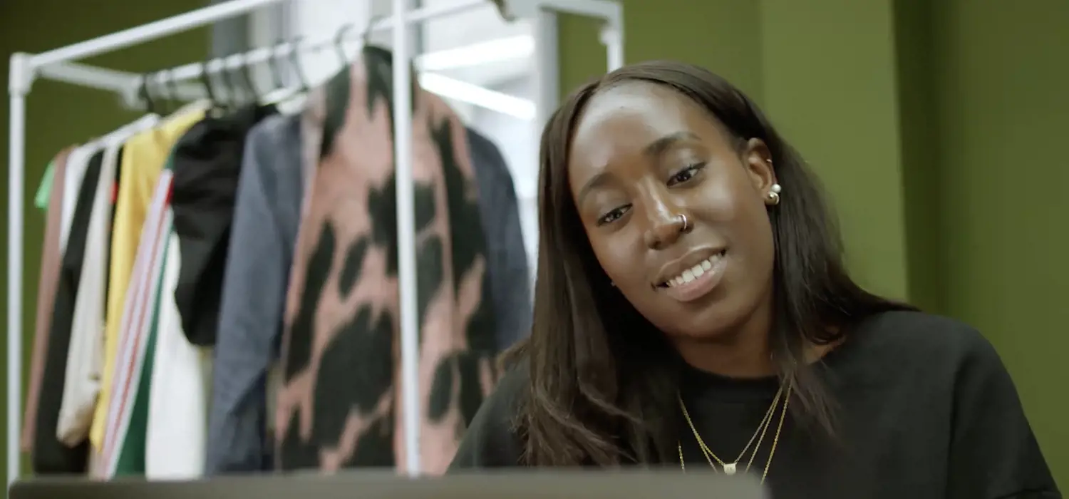 Tanda Kabanda: female software engineer smiles as she codes on a laptop with a clothes rail in the background