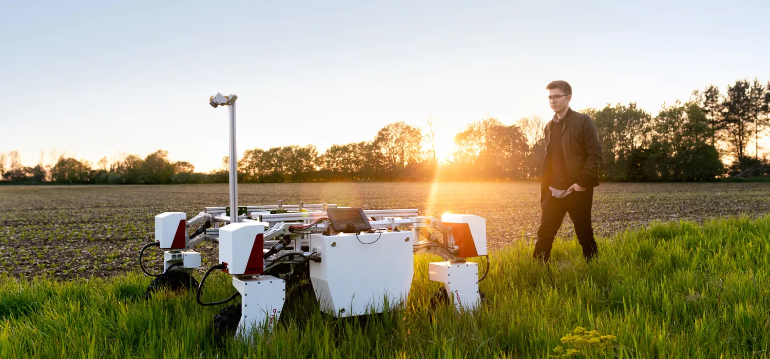 Male mechanical engineer with sustainable agricultural robot in field
