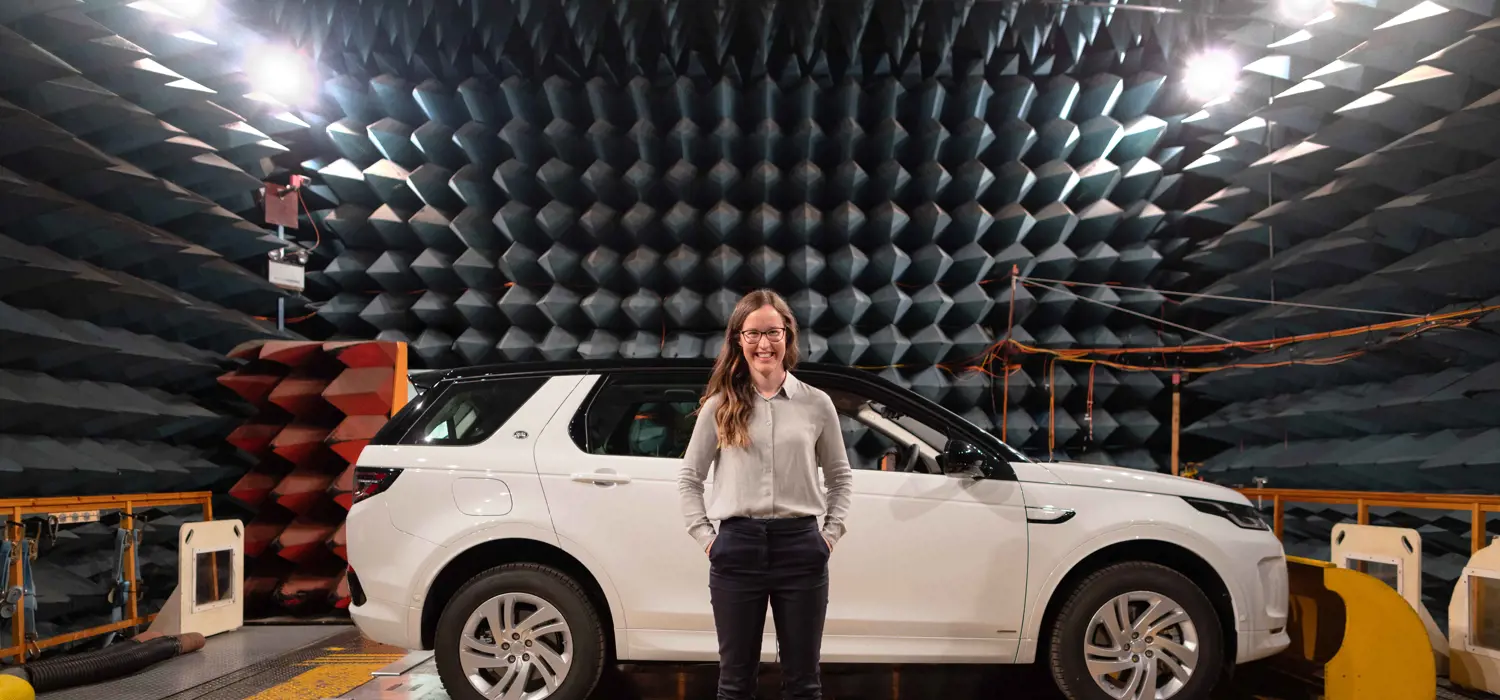 Female electronics and quality engineer stands with JLR vehicle in sound testing anechoic chamber