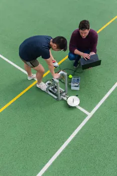 Male sports engineers test tennis equipment on a tennis court